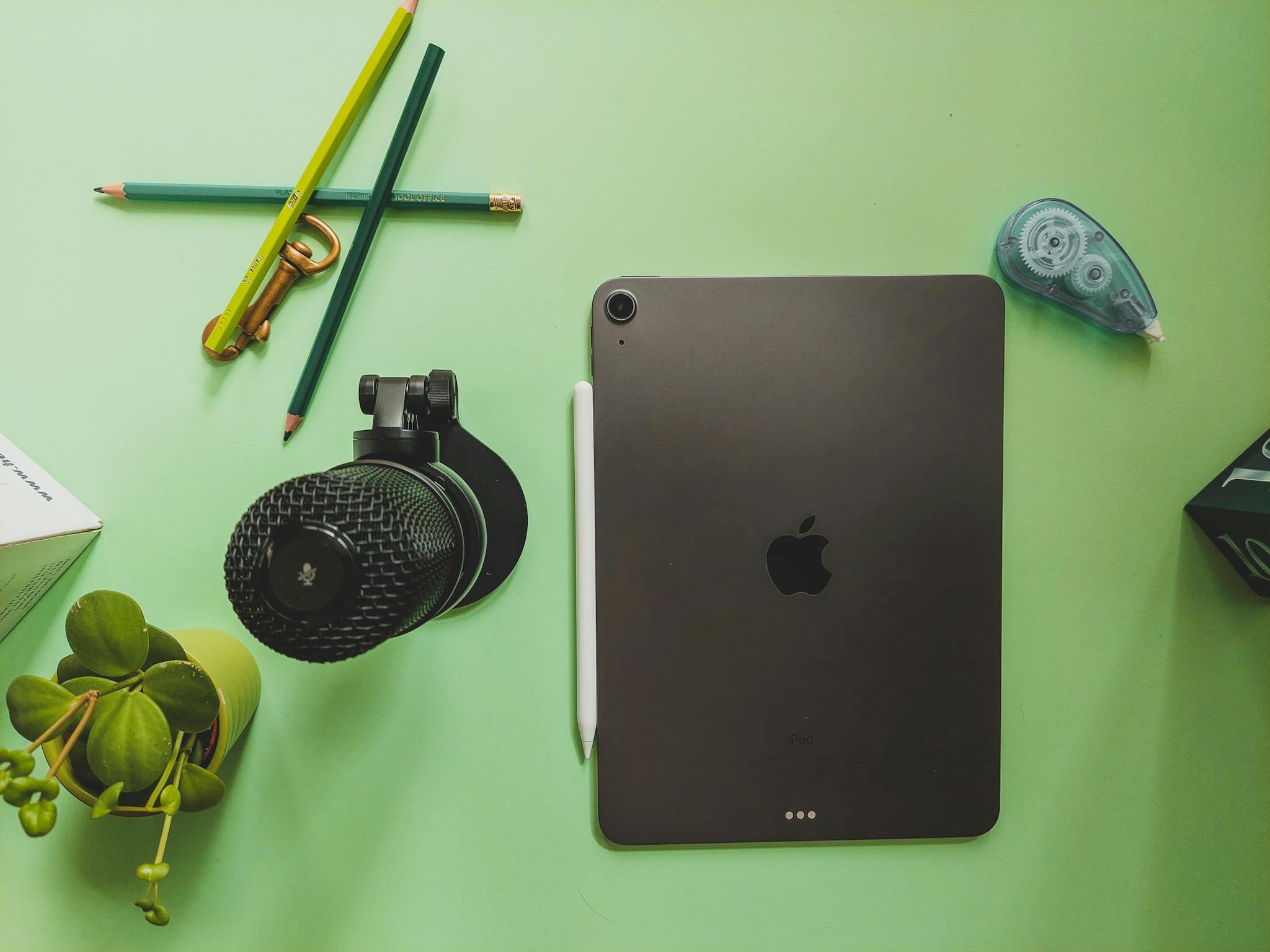 Flat lay of a workspace featuring a tablet, microphone, and stationery on a green desk.