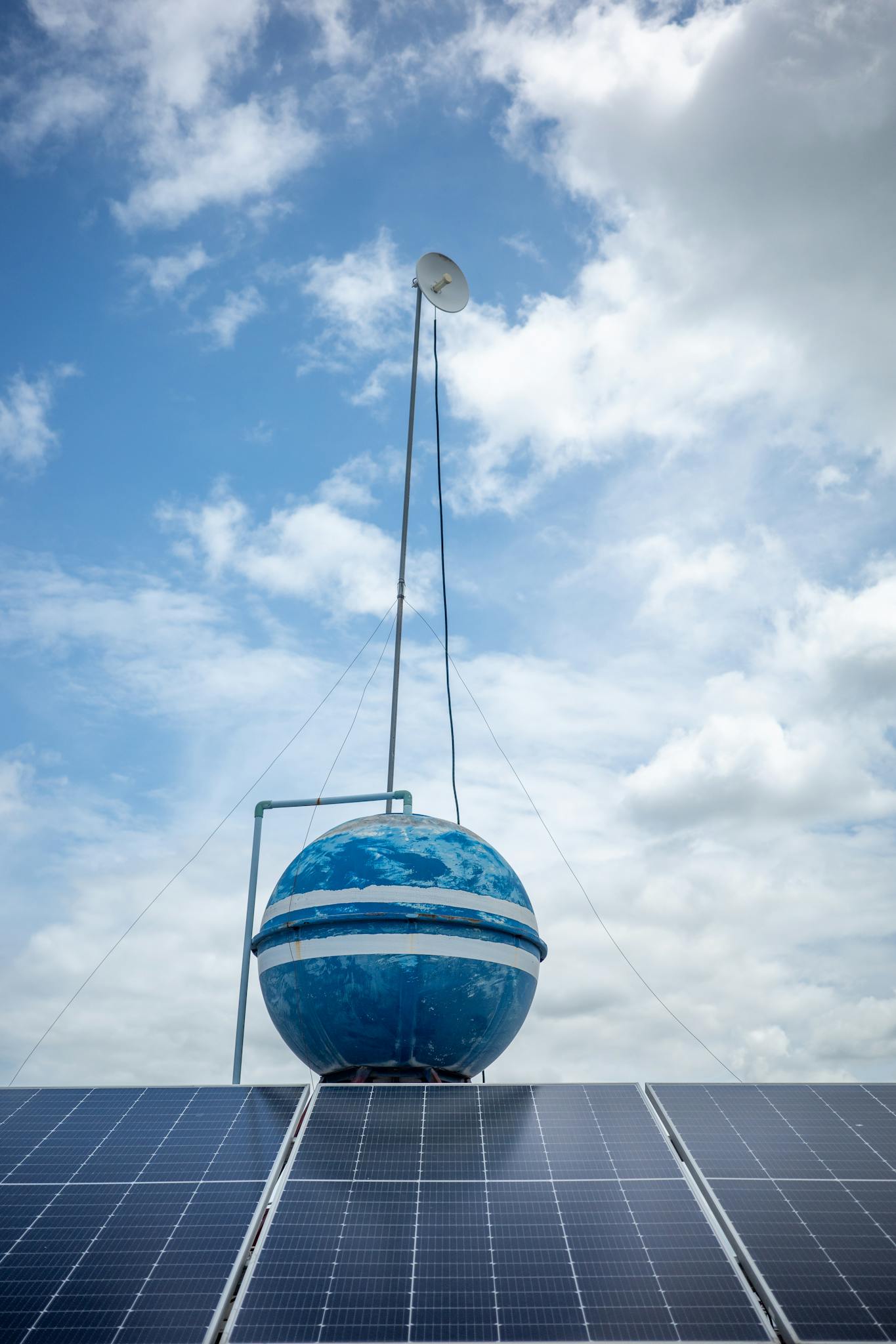 Vertical photo of solar panels with a blue globe structure and clear sky, symbolizing renewable energy.